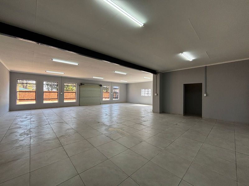 Spacious open-plan commercial area featuring tiled flooring, industrial lighting, and a large roller shutter door, suitable for various business or storage applications.