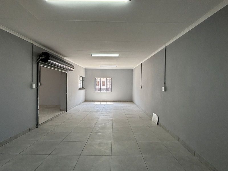 A clean, empty commercial utility space featuring tiled flooring, fluorescent lighting, and a secure roller shutter door entrance.