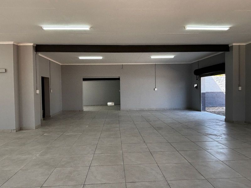 Spacious open-plan commercial area featuring neutral tiled flooring, modern grey walls, overhead fluorescent lighting, and a convenient roller shutter door access.
