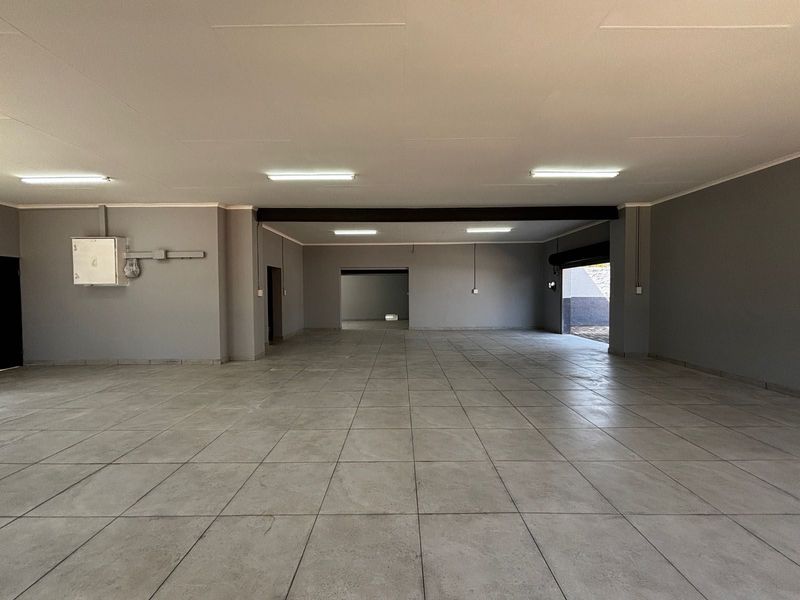 A spacious, open-plan commercial interior featuring neutral grey walls, large format floor tiles, and industrial lighting, suitable for various business or retail applications.