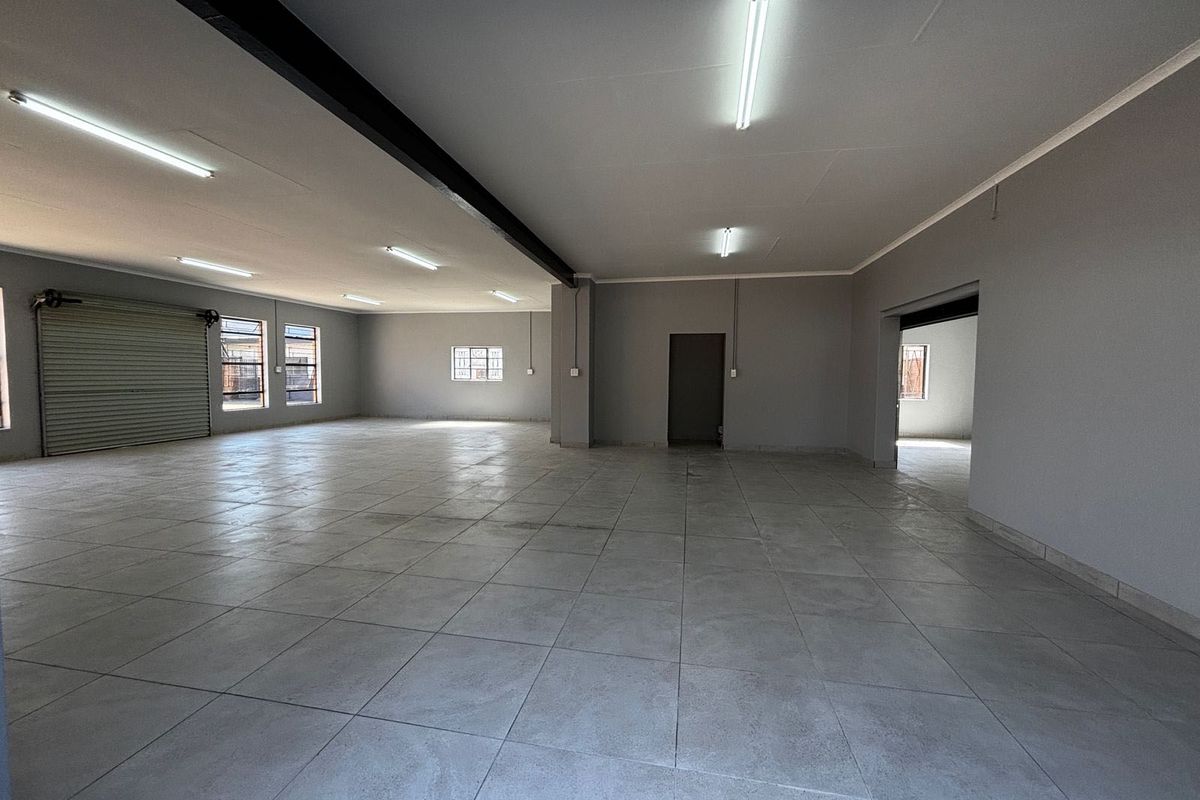 Spacious open-plan commercial area featuring neutral grey walls, durable tiled flooring, and a large roller shutter door for easy access.