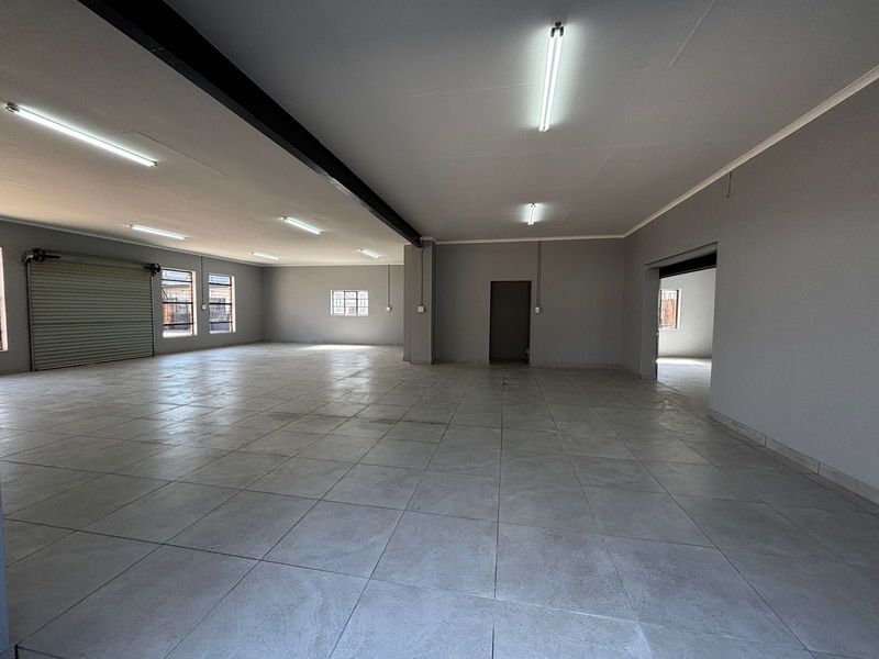 Spacious open-plan commercial area featuring neutral grey walls, durable tiled flooring, and a large roller shutter door for easy access.