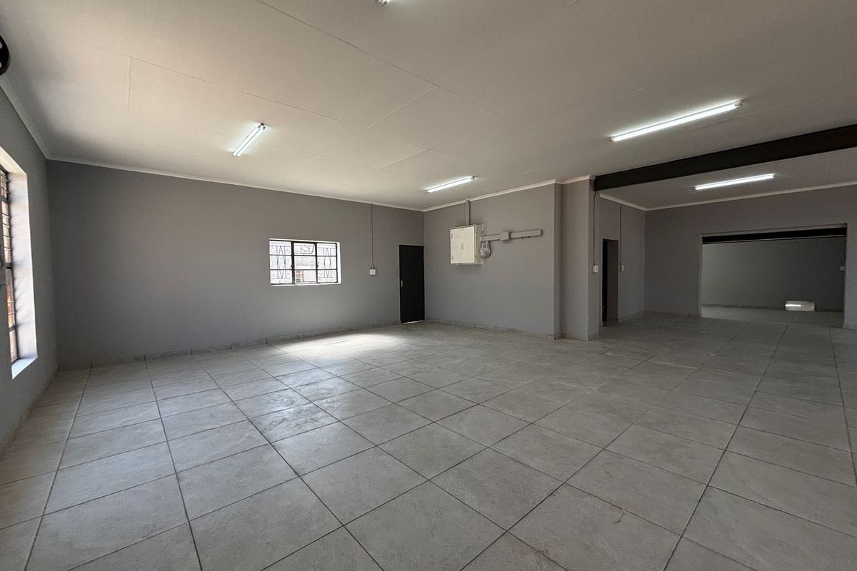 A spacious, empty open-plan commercial area featuring neutral grey walls, tiled flooring, and functional fluorescent lighting, suitable for various business or office configurations.