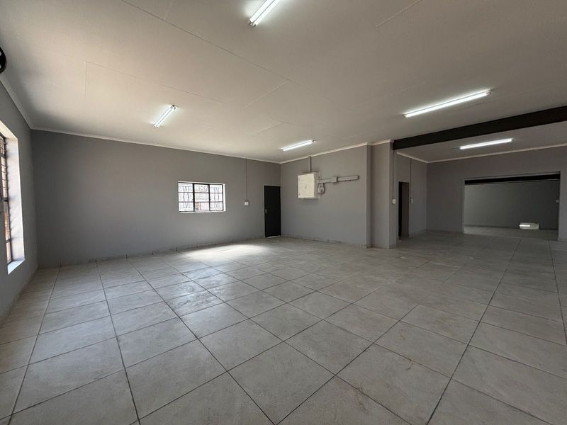 A spacious, empty open-plan commercial area featuring neutral grey walls, tiled flooring, and functional fluorescent lighting, suitable for various business or office configurations.