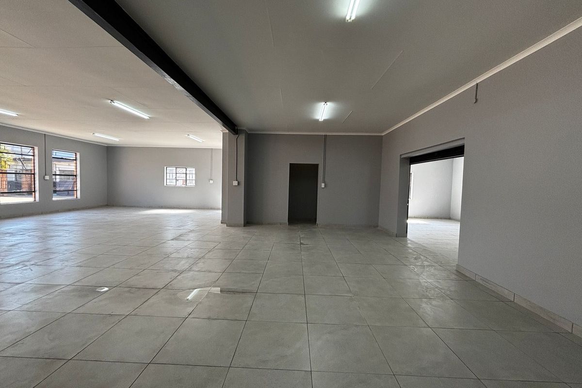 A spacious, open-plan commercial interior featuring neutral grey walls, tiled flooring, and bright fluorescent lighting, suitable for various business or retail applications.