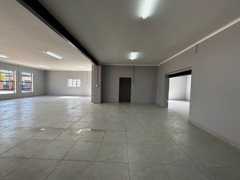 A spacious, open-plan commercial interior featuring neutral grey walls, tiled flooring, and bright fluorescent lighting, suitable for various business or retail applications.
