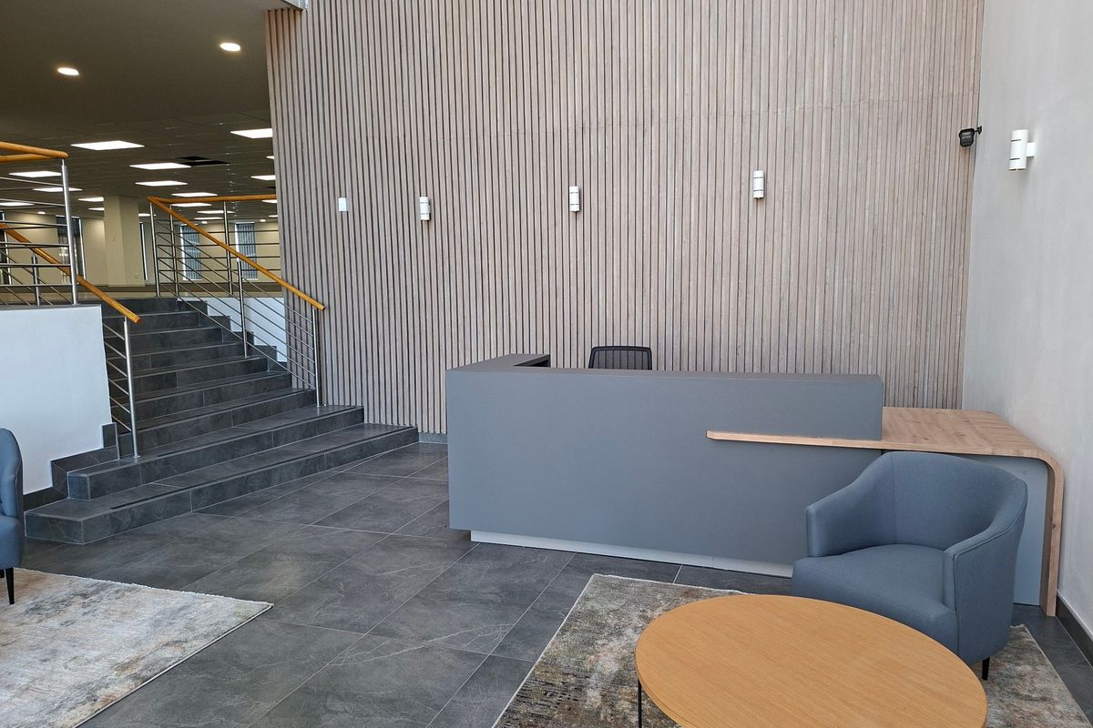 Modern commercial entrance lobby featuring a slatted timber feature wall, built-in reception desk, and a tiled staircase with contemporary handrails.