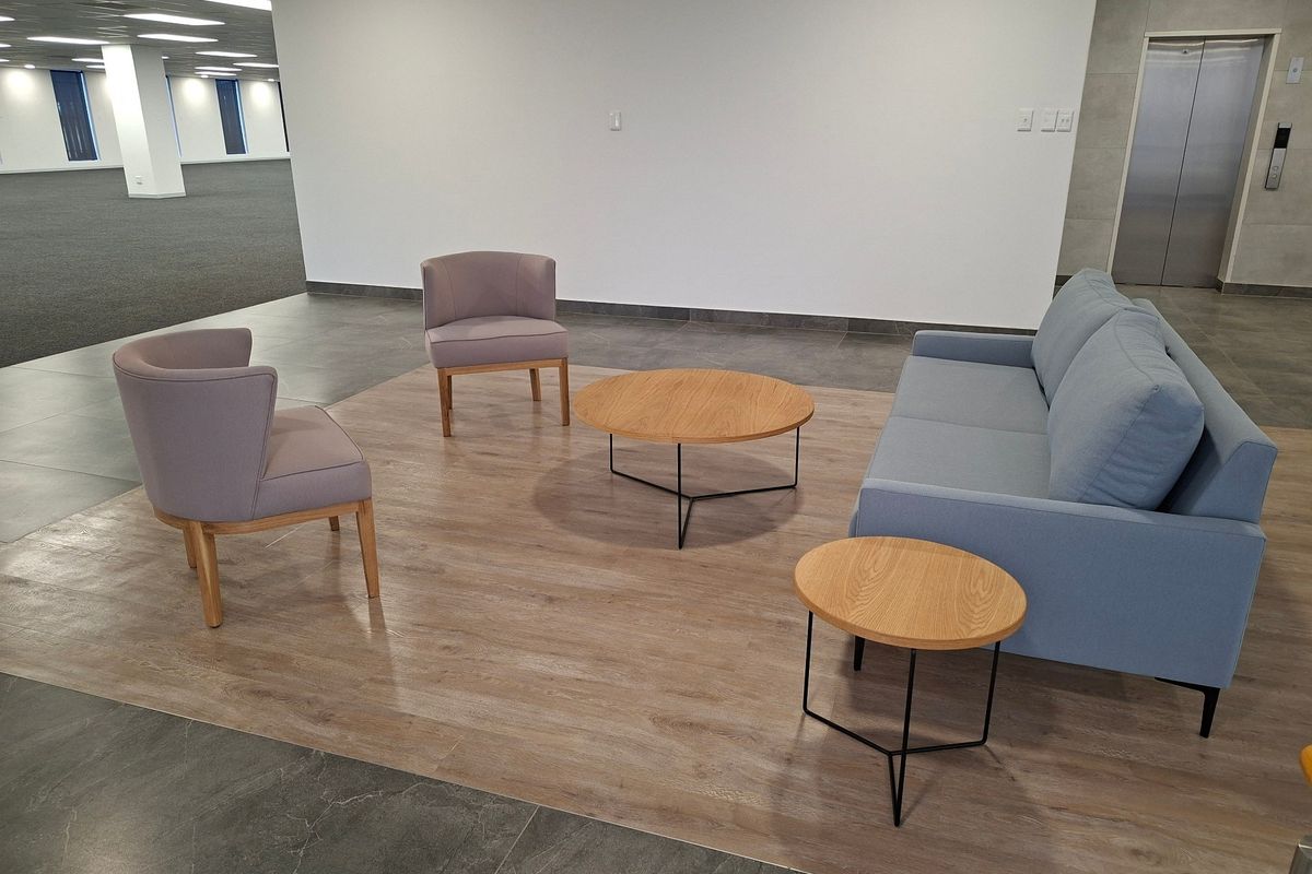 Modern open-plan commercial office space featuring a mix of tiled and wood-look flooring, recessed ceiling lighting, and direct elevator access.