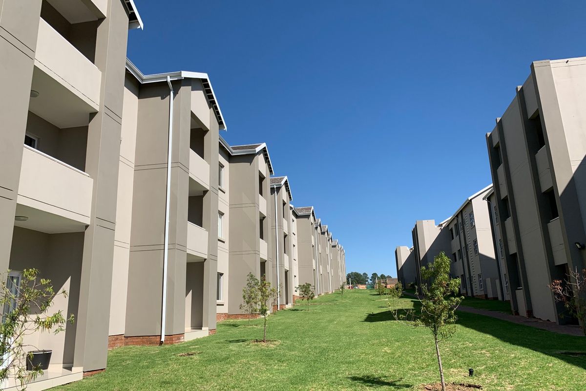 A view of the rear exterior of the apartment complex, featuring modern building facades, private balconies, and well-maintained communal green spaces.