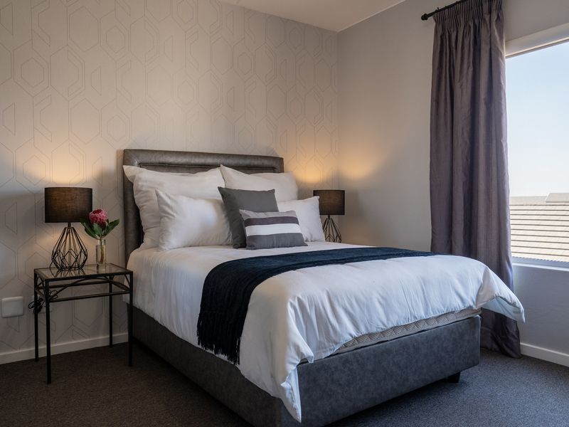 A well-maintained bedroom featuring patterned wallpaper, neutral carpeting, and a window with curtain fixtures, offering a comfortable and modern living space.