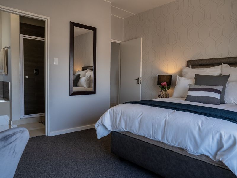 A well-maintained bedroom featuring patterned wallpaper, carpeted flooring, and an adjoining en-suite bathroom with a shower enclosure.