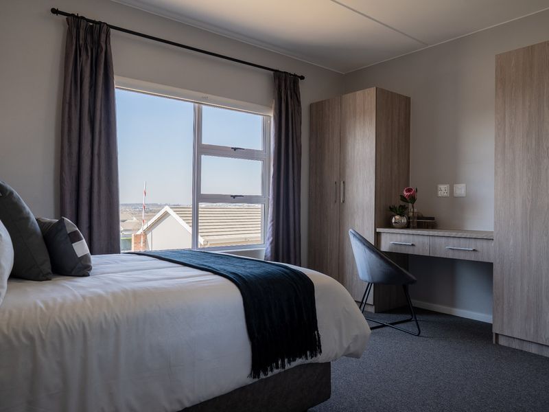 A well-maintained bedroom featuring built-in cabinetry, a desk, carpeted flooring, and a window with views of the surrounding neighborhood.