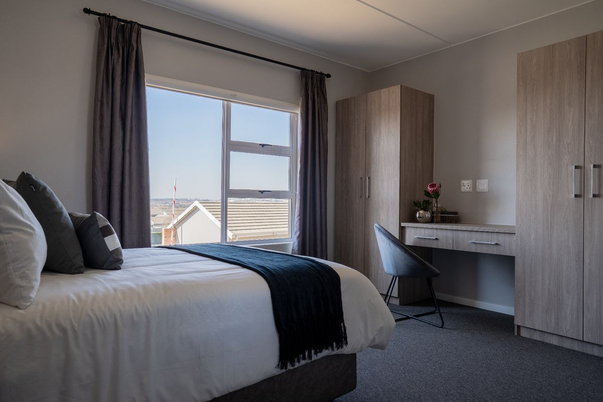 A well-maintained bedroom featuring built-in cabinetry, a desk, carpeted flooring, and a window with views of the surrounding neighborhood.