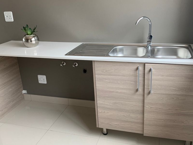 A clean and modern laundry area featuring a stainless steel double sink, chrome mixer tap, and ample laminate cabinetry with stone-look countertop.