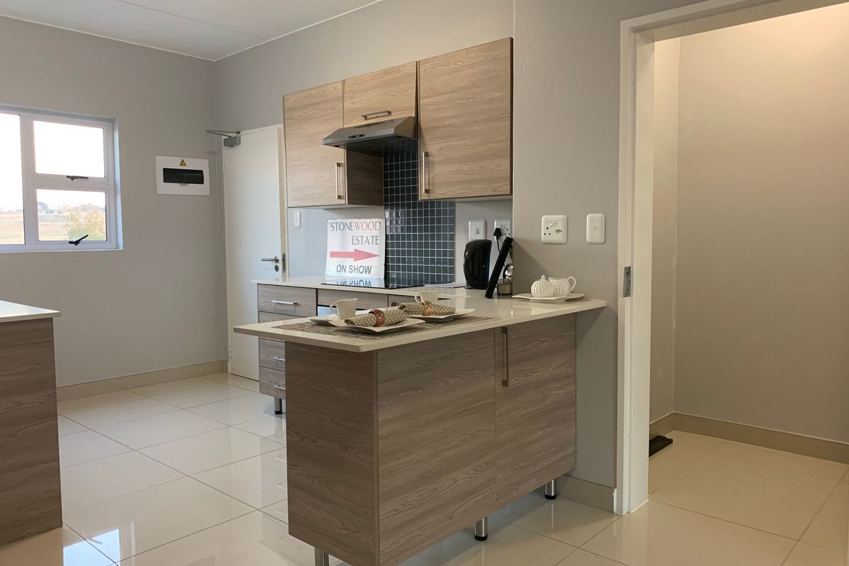 Modern kitchen featuring light wood-grain cabinetry, stone-look countertops, a tiled splashback, and sleek ceramic floor tiles in an open-plan layout.