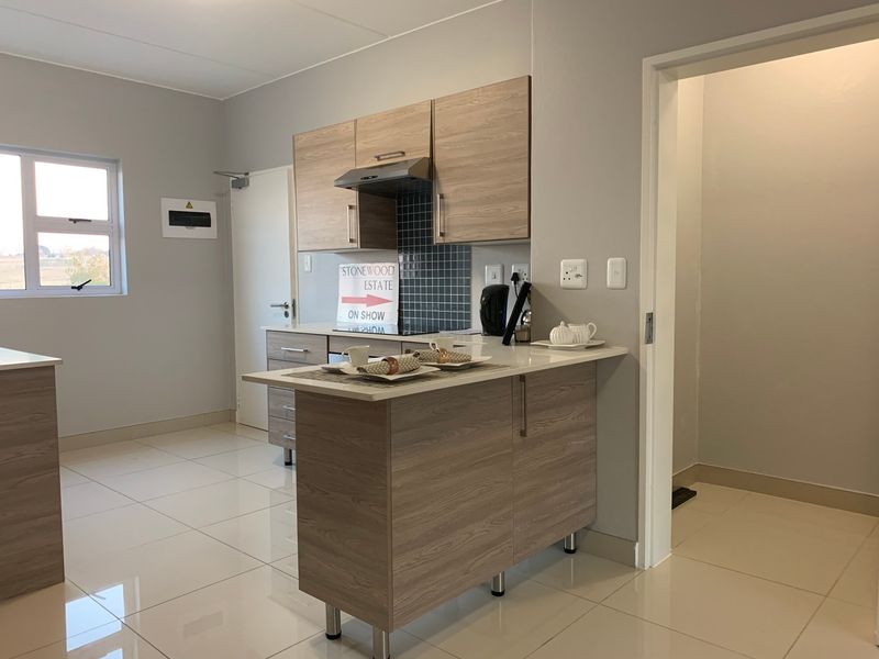 Modern kitchen featuring light wood-grain cabinetry, stone-look countertops, a tiled splashback, and sleek ceramic floor tiles in an open-plan layout.