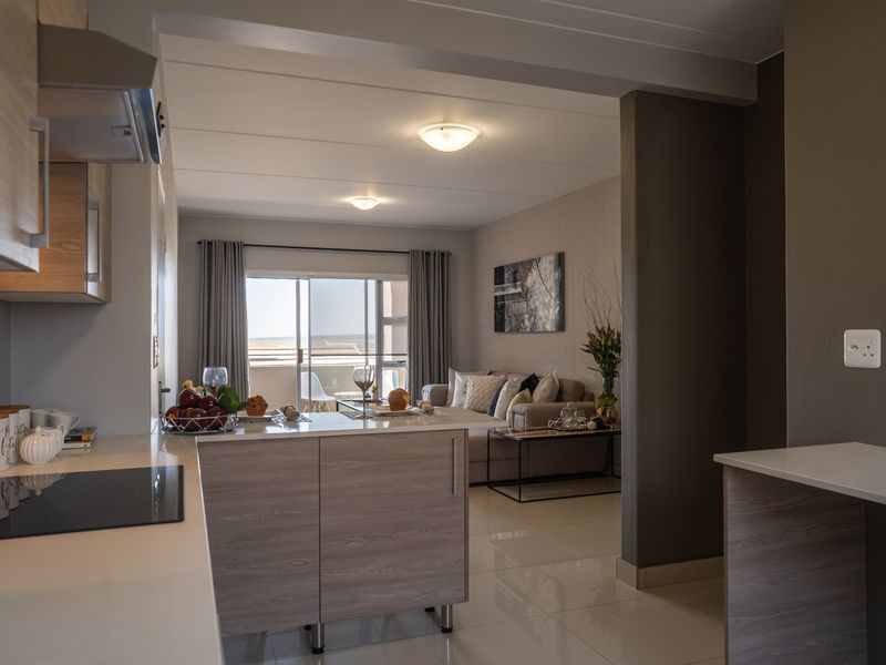 Modern open-plan kitchen and living area featuring sleek cabinetry, integrated hob, and sliding doors leading to a balcony with natural light.