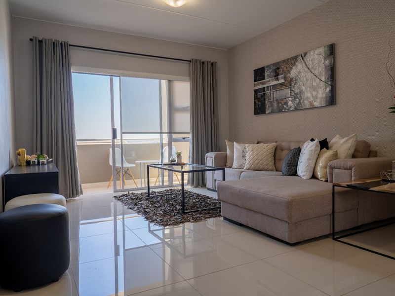 Modern living room featuring polished tile flooring, textured accent wall, and large sliding glass doors providing access to a private balcony.