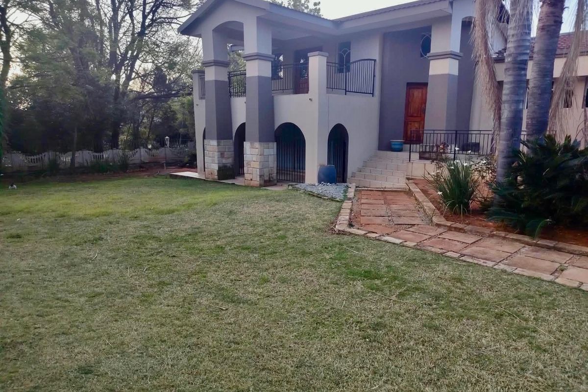 Rear view of a two-story house featuring stone-clad pillars, arched lower level architecture, an upper balcony with iron railings, and a landscaped garden.