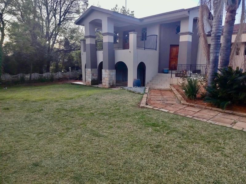 Rear view of a two-story house featuring stone-clad pillars, arched lower level architecture, an upper balcony with iron railings, and a landscaped garden.