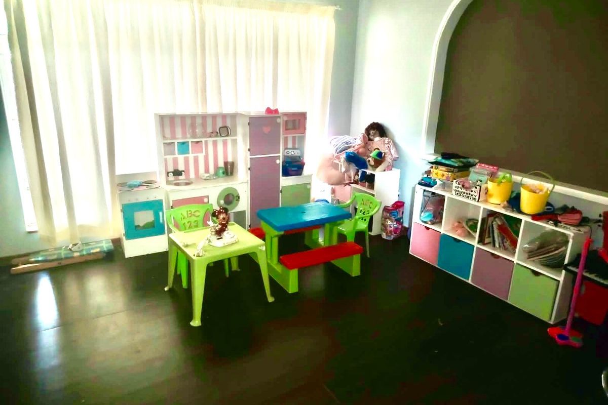 A bedroom featuring laminate flooring and a large window with curtain rails, currently utilized as a play area.