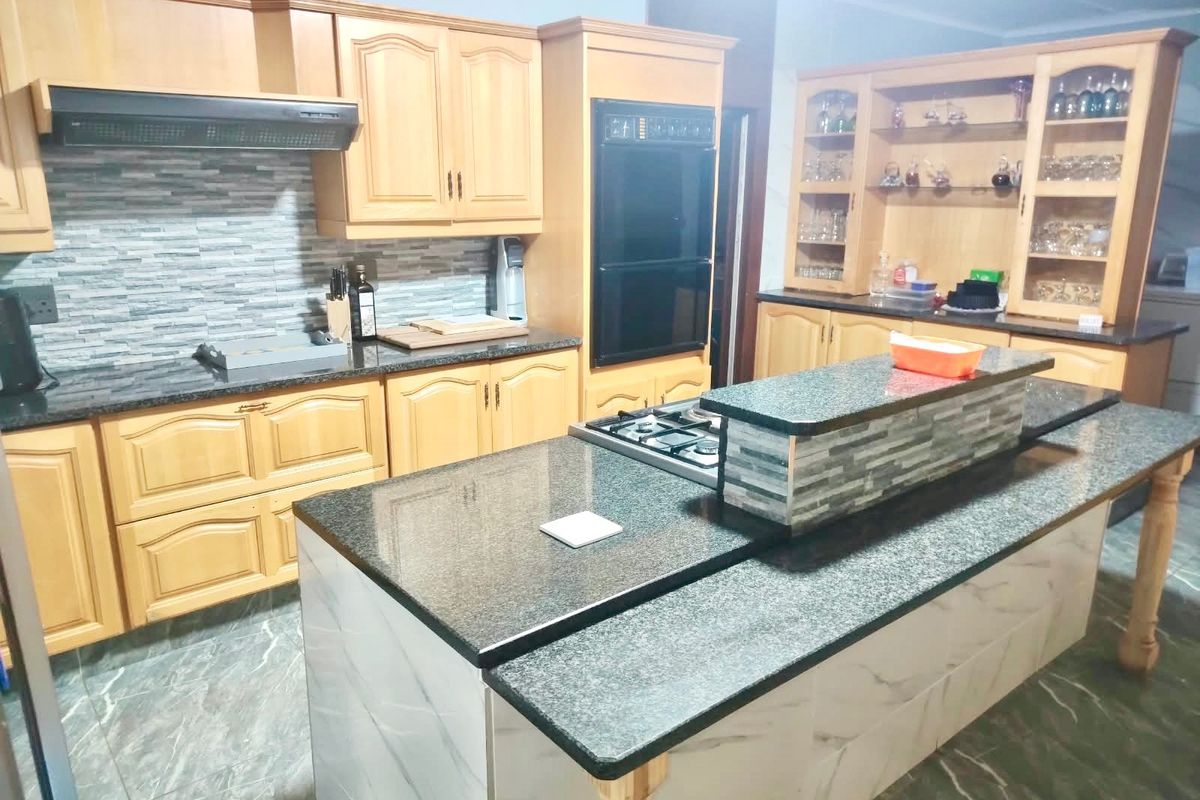 Spacious kitchen featuring granite countertops, a central island with a gas cooktop, built-in oven, and ample wooden cabinetry with glass display sections.
