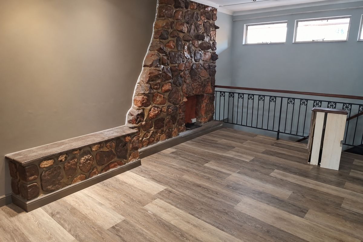 Spacious living area featuring a prominent stone fireplace, stone hearth, modern laminate flooring, and a decorative wrought iron balustrade overlooking the lower level.