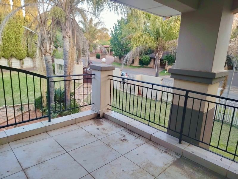 A covered balcony featuring tiled flooring and metal balustrades, overlooking the front garden and street area.