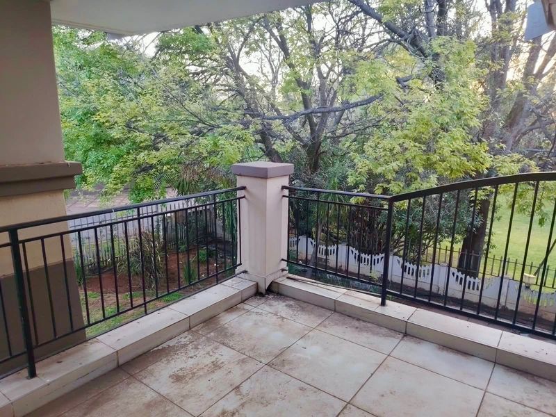 A covered balcony featuring tiled flooring and a metal balustrade, overlooking a garden area with mature trees.