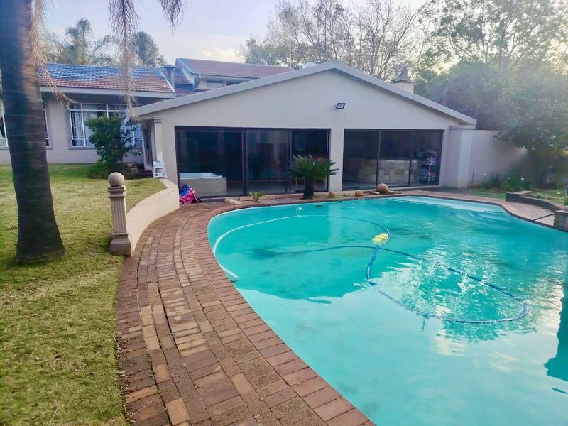 A well-maintained backyard featuring a swimming pool with brick paving, a retaining wall, and a covered patio area with large sliding glass doors.