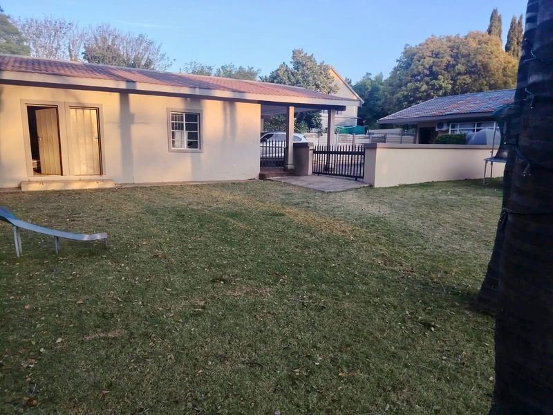 Rear view of the property featuring a covered patio, paved walkway, and a spacious lawn enclosed by a perimeter wall and gate.