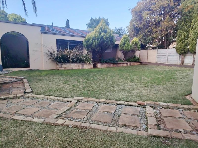 A rear garden view featuring a stone paved walkway, raised planter beds, and a well-defined lawn area enclosed by a boundary wall.