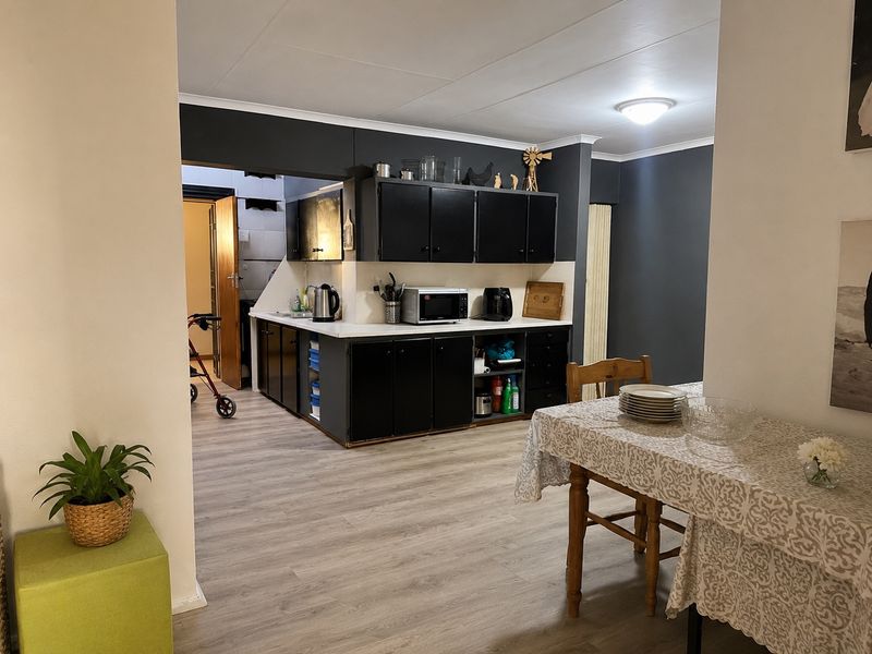 Open plan living and kitchen area featuring dark cabinetry, light laminate flooring, and a functional layout connecting to a secondary utility space.