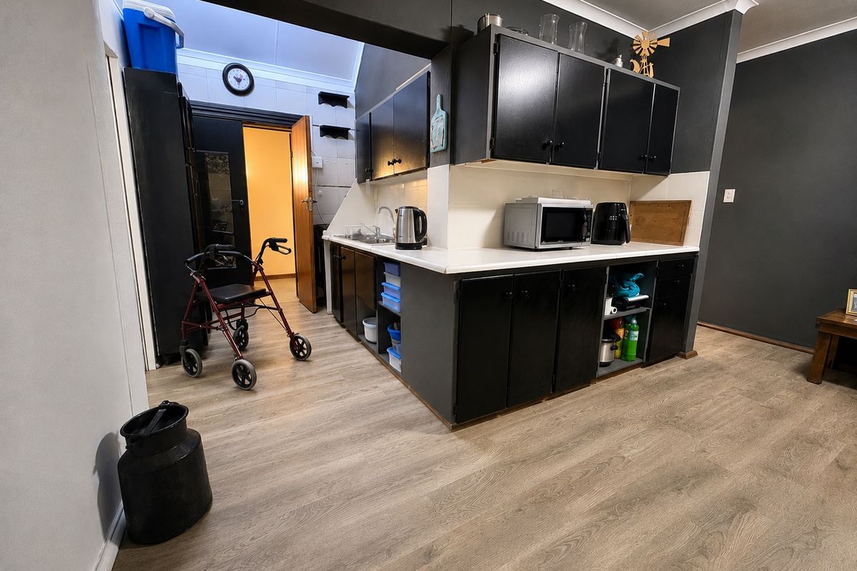 A functional kitchen area featuring dark cabinetry, white countertops, a stainless steel sink, and modern wood-look vinyl flooring.