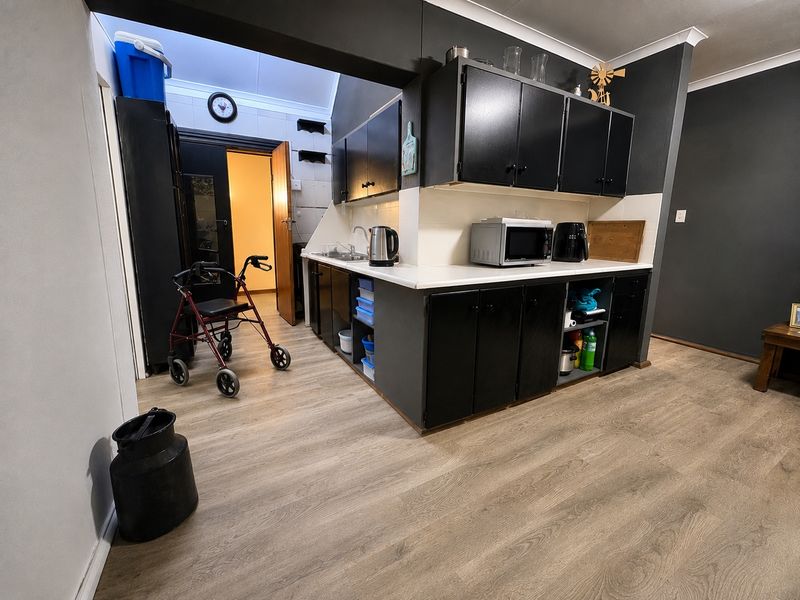 A functional kitchen area featuring dark cabinetry, white countertops, a stainless steel sink, and modern wood-look vinyl flooring.