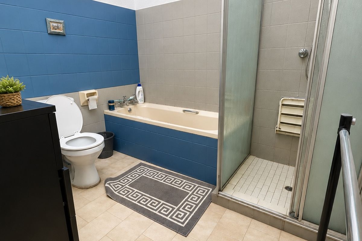 A functional bathroom featuring a bathtub, separate shower enclosure, and toilet with neutral and blue tiled wall finishes.