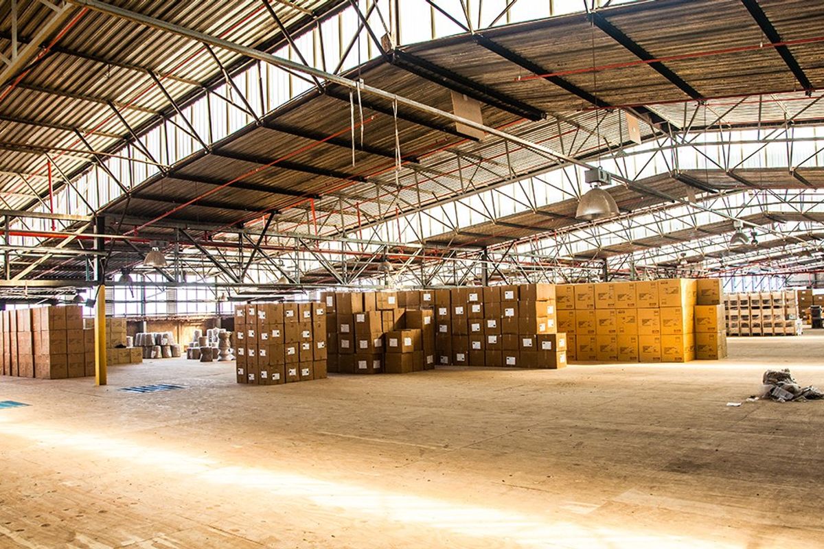 Large industrial warehouse space featuring high-clearance steel truss roofing, concrete flooring, and integrated fire sprinkler systems, suitable for storage or manufacturing operations.