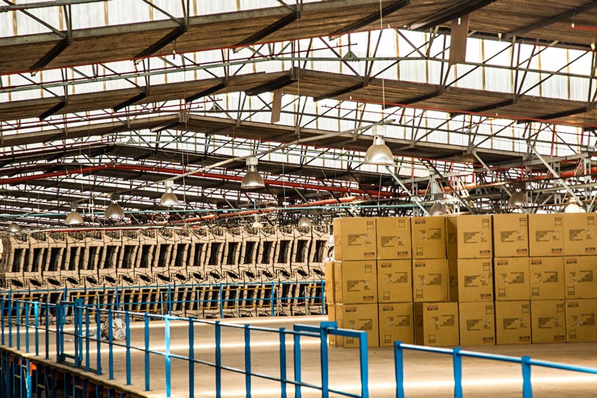 Spacious industrial warehouse interior featuring high exposed steel truss ceilings, translucent roofing for natural light, and durable concrete flooring with safety railings.