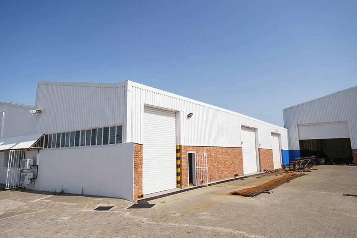 Industrial warehouse facility featuring multiple roller shutter doors, brick and metal cladding exterior, and a paved yard area.