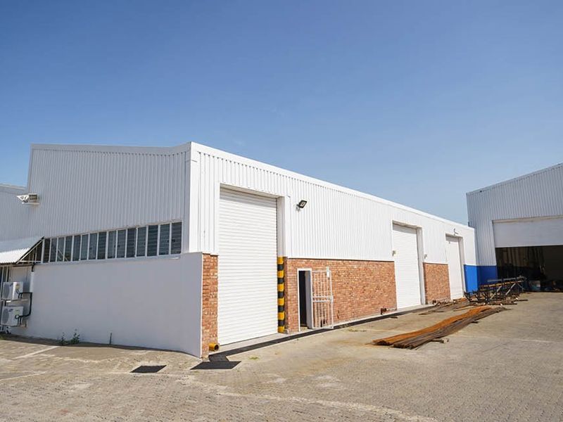 Industrial warehouse facility featuring multiple roller shutter doors, brick and metal cladding exterior, and a paved yard area.