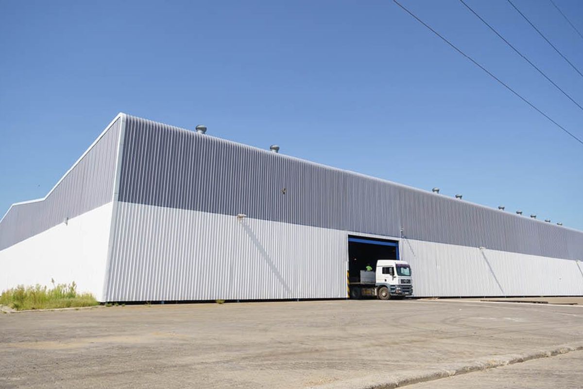 A large industrial warehouse featuring corrugated metal cladding, a spacious paved yard, and a high-clearance roller door entrance.