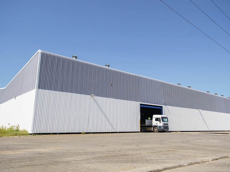 A large industrial warehouse featuring corrugated metal cladding, a spacious paved yard, and a high-clearance roller door entrance.