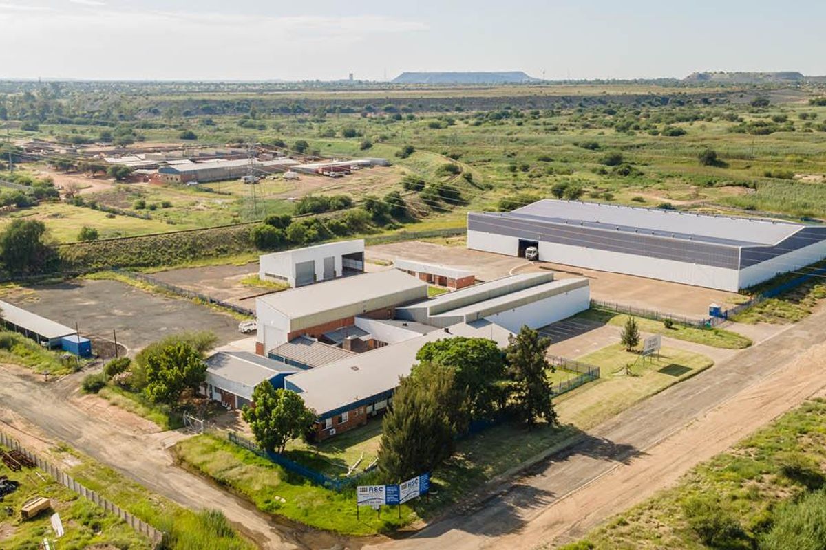 Aerial view of an industrial property complex featuring multiple warehouse structures, paved yard areas, and perimeter fencing in a spacious outdoor setting.