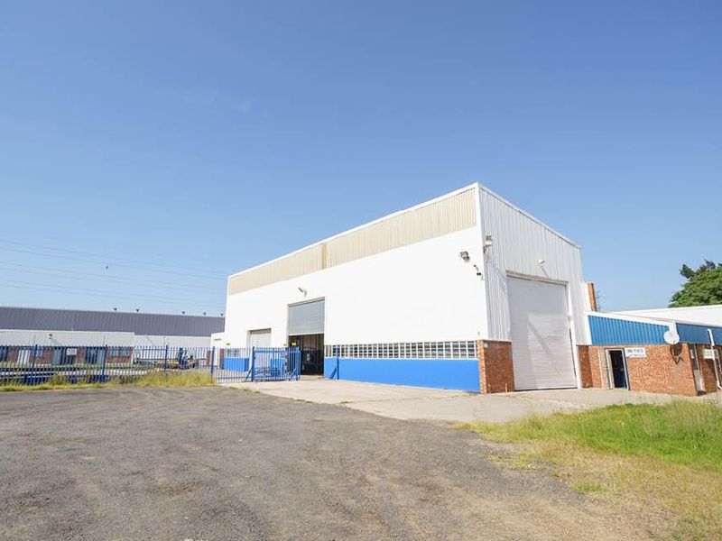 Industrial warehouse facility featuring large roller shutter doors, metal cladding, and secure perimeter fencing with an expansive concrete yard area.