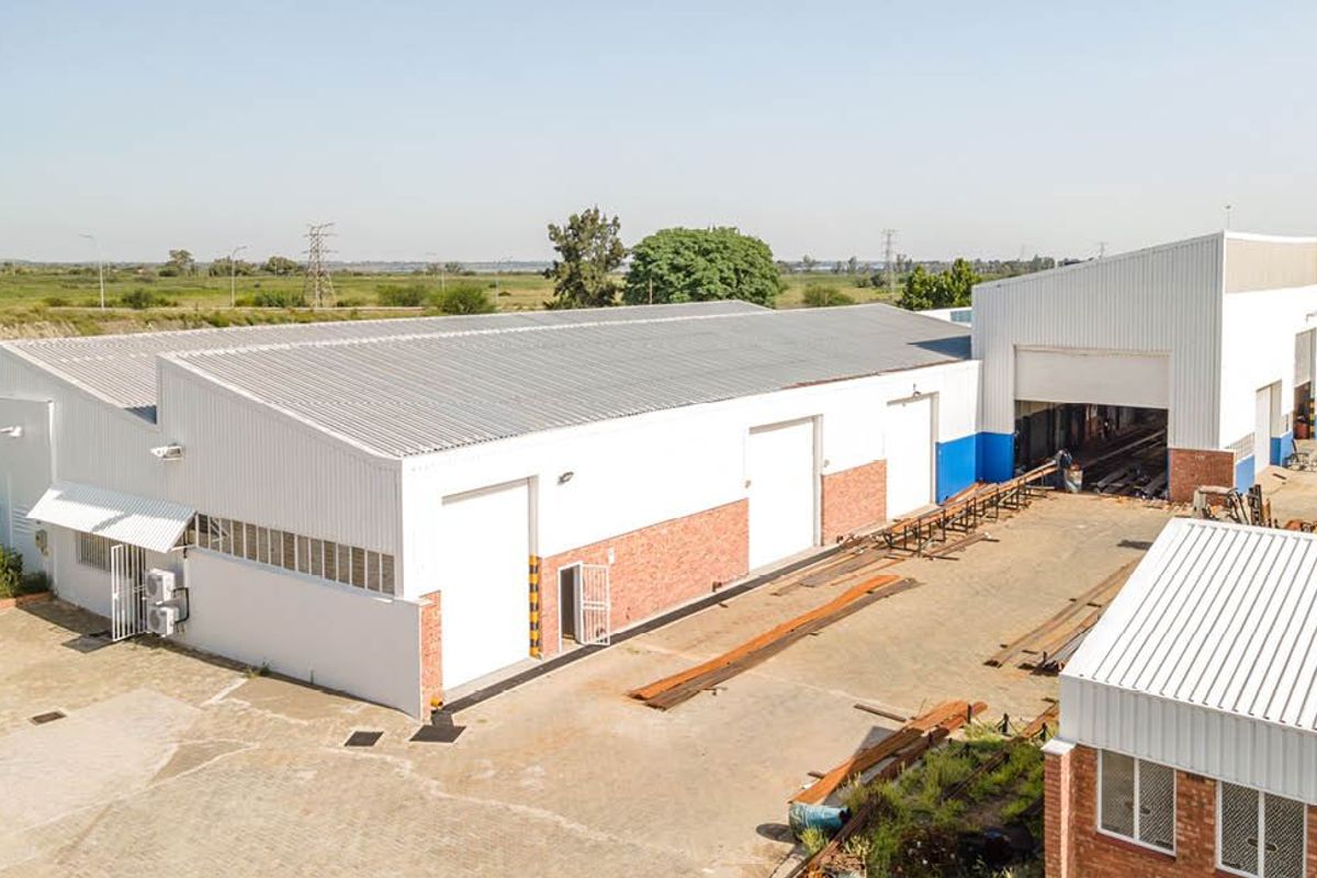 Aerial view of an industrial warehouse facility featuring corrugated metal roofing, multiple roller shutter doors, and a spacious paved yard area.
