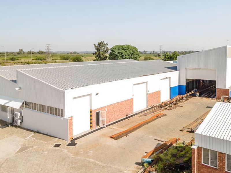 Aerial view of an industrial warehouse facility featuring corrugated metal roofing, multiple roller shutter doors, and a spacious paved yard area.