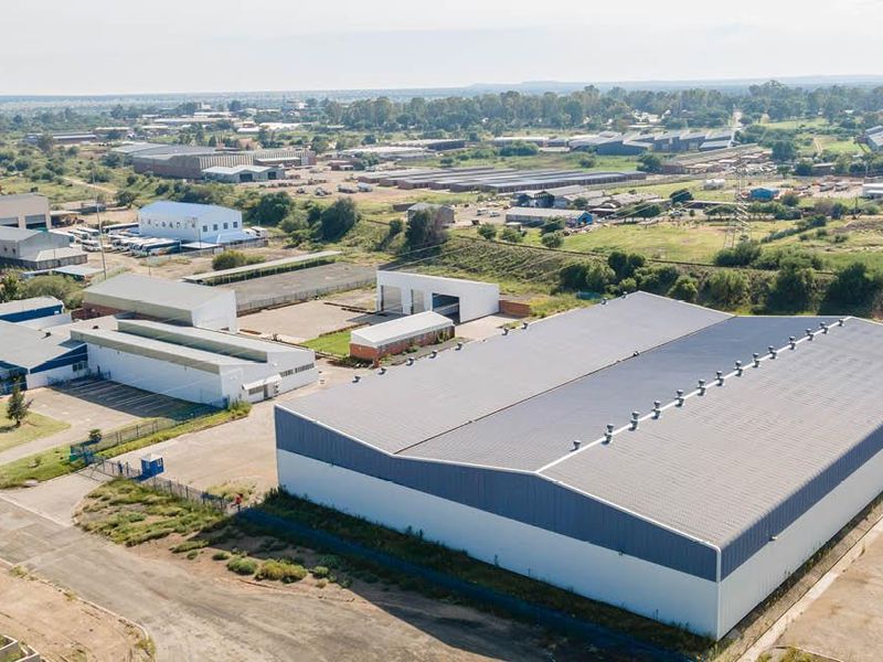 Aerial view of an industrial property featuring a large warehouse building with metal roofing, situated within a developed industrial park with paved yard space.