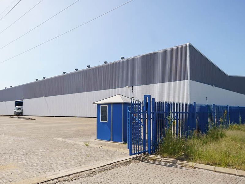 Large industrial warehouse facility featuring corrugated metal cladding, a paved yard, secure perimeter fencing, and a dedicated security guard hut.