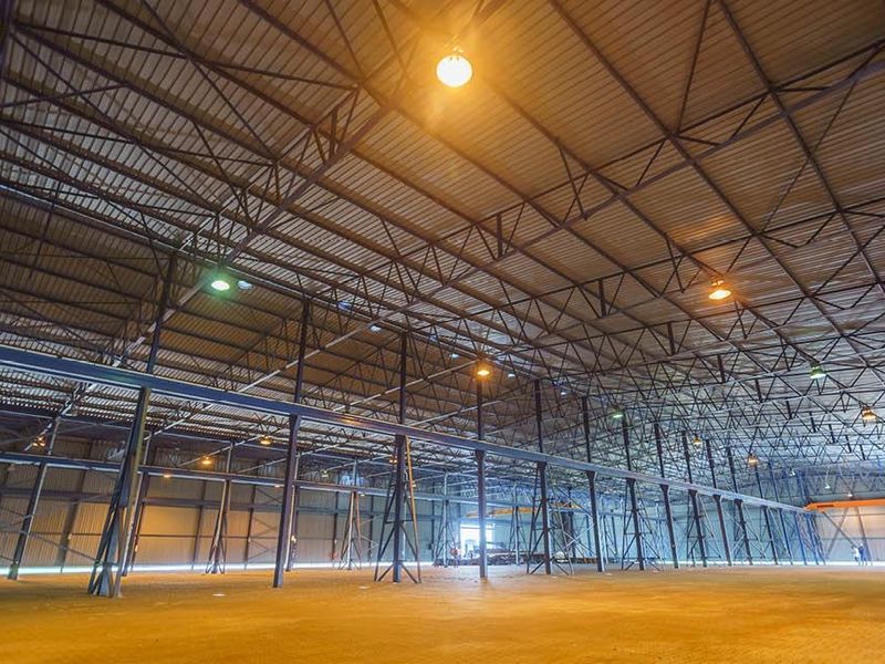 A large, open-plan industrial warehouse space featuring high ceilings with exposed steel trusses, metal cladding, and durable concrete flooring.