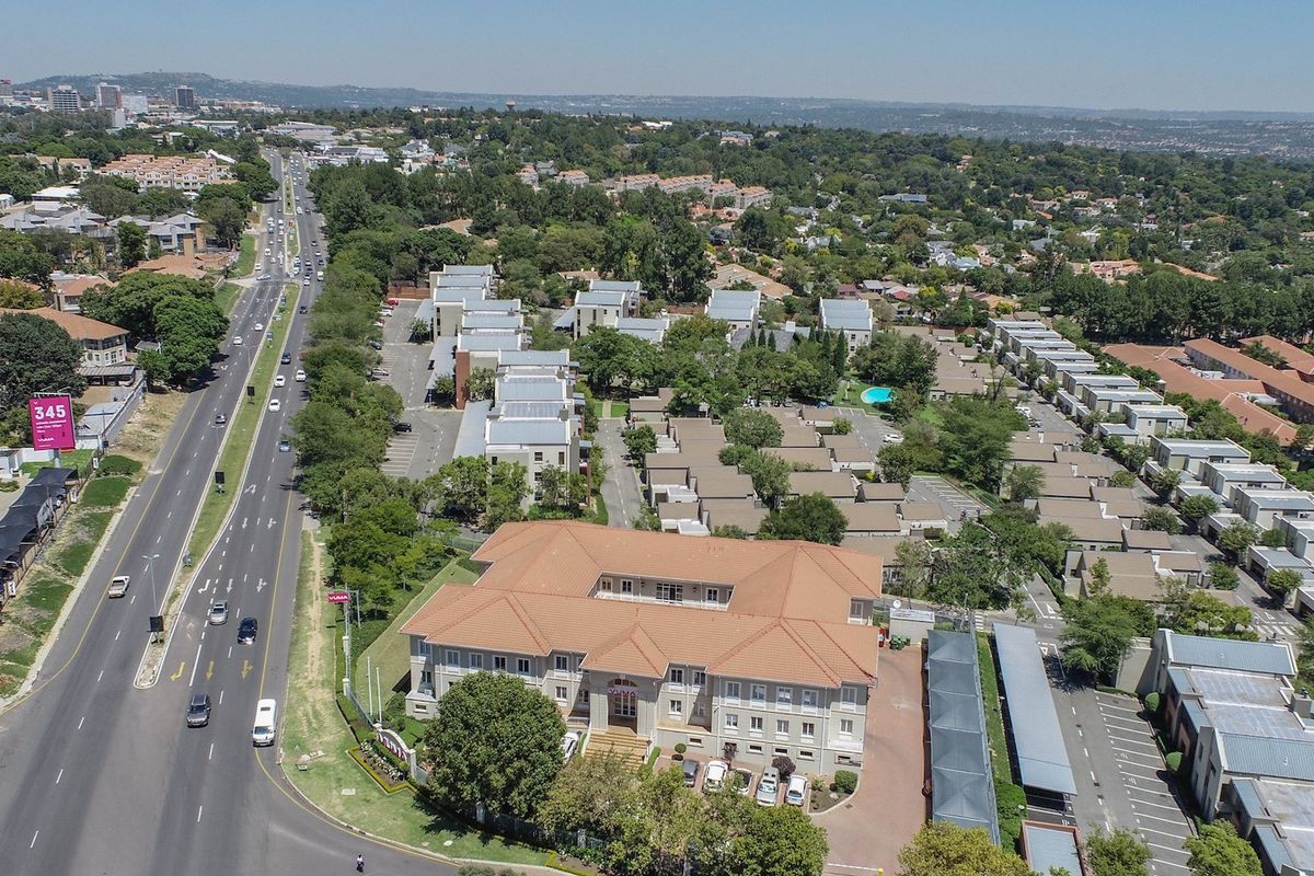 Aerial view of a commercial office complex featuring a main building with a tiled roof, extensive parking facilities, and landscaped grounds.
